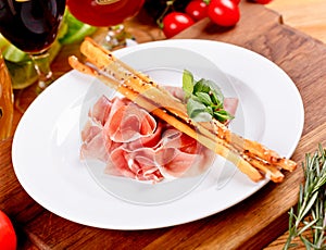 Jamon Serrano, Prosciutto Crudo or Parma ham and breadsticks on white plate photo