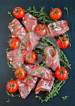 Jamon Serrano sliced with small cherry tomatoes and fresh thyme on black stone background. Top view