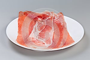 Jamon slices on dish on gray background, side view closeup