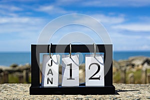 Jan 12 calendar date text on wooden frame with blurred background of ocean