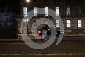 Part of Monument to the Women of World War II on Whitehall in London at night with car passing in motion blur
