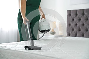 Janitor cleaning mattress with professional equipment in bedroom