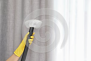 Janitor removing dust from curtain with steam cleaner