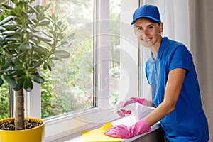 Janitorial cleaning services. smiling female worker disinfecting apartment windowsill
