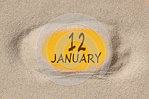 January 12. 12th day of the month, calendar date. Hole in sand. Yellow background is visible through hole