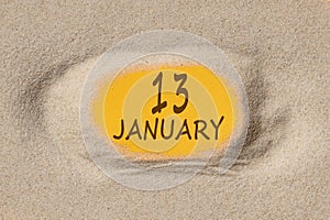 January 13. 13th day of the month, calendar date. Hole in sand. Yellow background is visible through hole