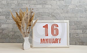 january 16. 16th day of month, calendar date. White vase with ikebana and photo frame with numbers on desktop, opposite