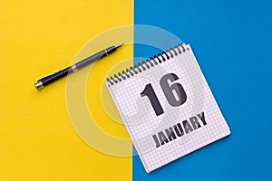January 16th. Day 16 of month. Calendar date. Notebook with a spiral and pen lies on a yellow-blue background