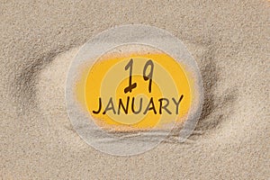 January 19. 19th day of the month, calendar date. Hole in sand. Yellow background is visible through hole