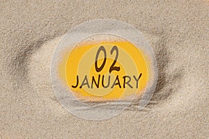 January 2. 2th day of the month, calendar date. Hole in sand. Yellow background is visible through hole