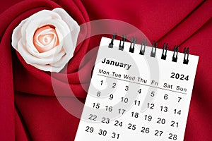 The January 2024 desk calendar and pink rose on red textile background