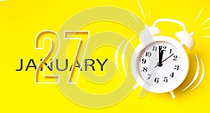 January 27th. Day 27 of month, Calendar date. White alarm clock with calendar day on yellow background. Minimalistic concept of