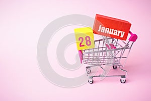 January 28th. Day 28 of month, Calendar date. Close up toy metal shopping cart with red and yellow box inside with Calendar date