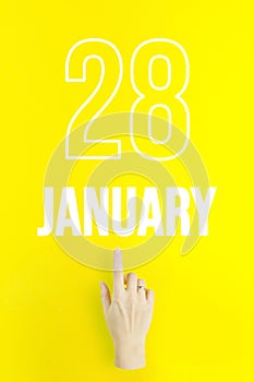 January 28th. Day 28 of month, Calendar date.Hand finger pointing at a calendar date on yellow background.Winter month, day of the