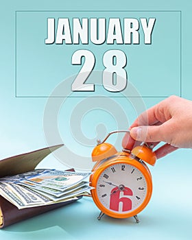 January 28th. Hand holding an orange alarm clock, a wallet with cash and a calendar date. Day 28 of month.