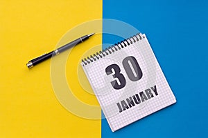 January 30th. Day 30 of month. Calendar date. Notebook with a spiral and pen lies on a yellow-blue background