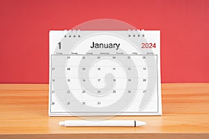 The January monthly desk calendar for 2024 year and pen on the wooden table with red color background