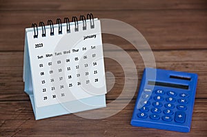 January 2023 white desk calendar with magnifying glass on wooden table. Calendar copy space