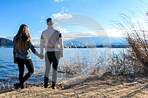 Japan - A couple holding hands at the side of Kawaguchiko Lake and admiring Mt Fuji