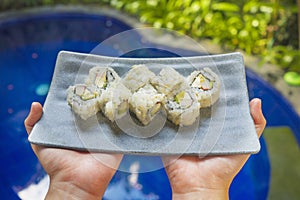 Japan gourmet cuisine - hands presenting delicious and delicate dish of Japanese sushi rolls in grey slate in traditional healthy