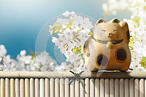 Japan Maneki Neko or Beckoning Cat standing on Bamboo Fence over