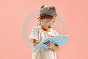 Japanese apperance child concentrating on writes to copybook, pen in hand, against pink background. photo