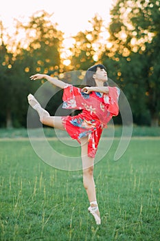 Japanese ballerina in red kimono stands in swallow pose