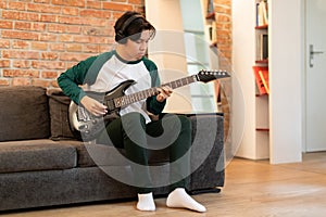 Japanese Boy Wearing Earphones Playing Chords On Electric Guitar Indoors
