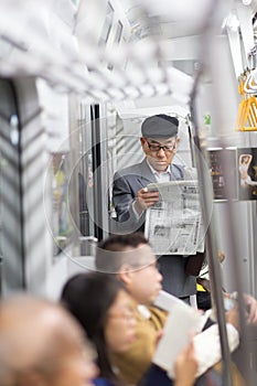 Japanese businessman taking ride to work in morning, standing inside public transport and reading newspaper.