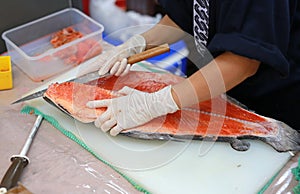 Japanese chef in restaurant slicing raw fish for salmon sushi. Chef preparing a fresh salmon on a cutting board