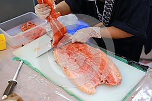 Japanese chef in restaurant slicing raw fish for salmon sushi. Chef preparing a fresh salmon on a cutting board