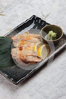 Japanese chicken grilled with sea salt served with sliced lemon and wasabi in stone rectangle plate on washi Japanese paper