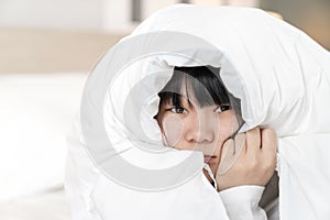 Japanese Chinese woman feels afraid and uncomfortable, she holds white blanket to cover her head on the bed