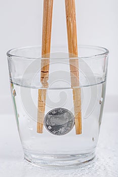 Japanese coin yen holding by wooden chopsticks in a glass of w