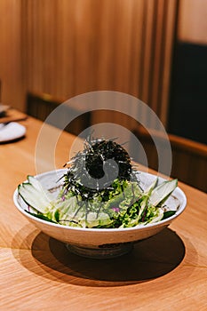 Japanese cucumber salad with lettuce, radish and dry seaweed served in a ceramic bowl on the wooden counter