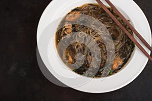 Japanese cuisine, soup with chashu pork, chives, sprouts, noodles and seaweed on the table under the sunlight. Old black rustic ba