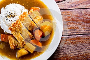 Japanese curry with rice, black sesame, carrot, potato and deep fries chicken in white dish on wooden table