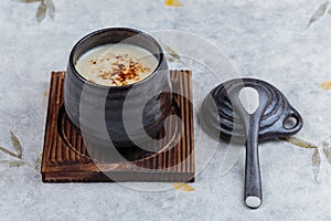 Japanese custard pudding torched caramel on top served in black ceramic cup on wooden plate with lid and spoon on washi.