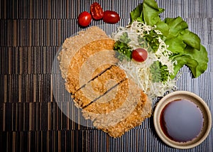 Japanese deep fried breaded pork cutlet served with shredded cabbage and tonkatsu sauce on black background. Stock photo