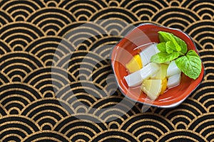 Japanese dessert of Annin-doufu with fruits pieces like and a mint leaf.