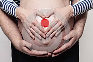 Japanese family concept. Man embracing pregnant woman belly and heart with flag of  Japan colors closeup