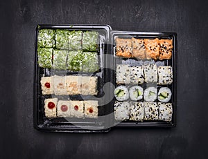 Japanese fast food, sushi set with two variousingredients in plastic containers on dark rustic background, top view