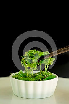 Japanese food concept. Fresh seaweed salad with sesame seeds in white bowl with chopstick on black background