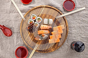 Japanese food restaurant sushi maki roll set on wooden round board with chopsticks on fabric grey background