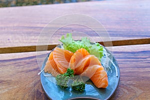 Japanese food sashimi salmon in black plate decoration with vegetable on wooden table.