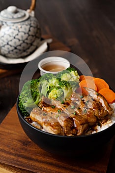 Japanese Food Style : Homemade Chicken Teriyaki grilled with rice , carrot , broccoli put on the black bowl and place on wooden