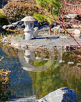 Japanese garden. A stone lamp stands among the bushes by the pond on the sand, like a garden decor. Trees, stones, a