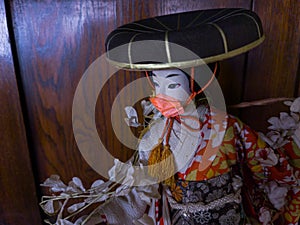 Japanese geisha doll wearing a reddish chinstrap in a wooden background