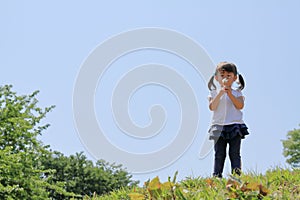 Japanese girl blowing dandelion seeds under the blue sky