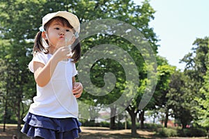 Japanese girl blowing dandelion seeds under the blue sky